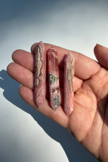 Three polished pink rhodochrosite crystal points held in a person's hand against a light gray background.