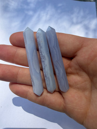 Three pale blue-gray pointed crystal points held in a person's hand against a light blue sky background.