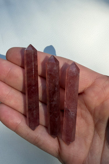 Three pointed berry reddish-brown crystal points held in a person's hand against a plain light background.