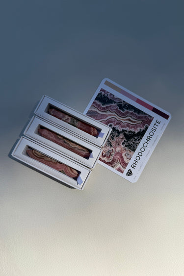 Three Banded Pink Rhodochrosite wands inside their Stoned Crystals packaging with a card explaining the crystal's properties.
